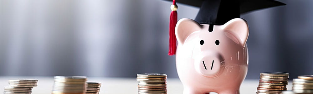 Piggy bank with graduation cap on table with stacks of coins