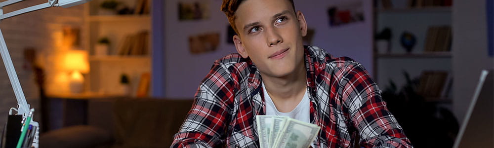 College student sitting at his desk holding cash