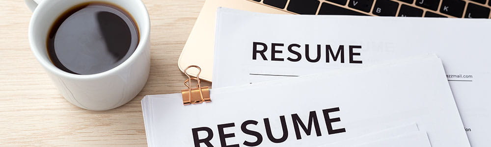Resumes on a desk with a laptop