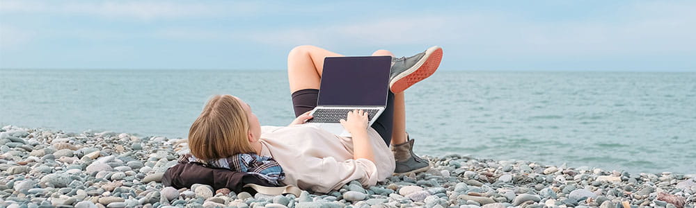 Girl laying on the beach using a laptop