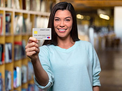 Female student holding out a credit while standing in the library.