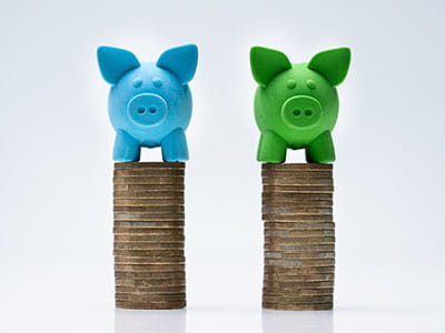 Blue and Green piggy bank each atop it's own stack of coins