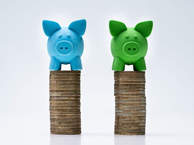 Blue and Green piggy banks each atop its own stack of coins