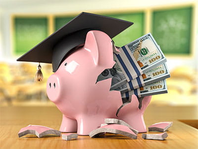 Piggy bank wearing graduation cap with cash bursting out of it