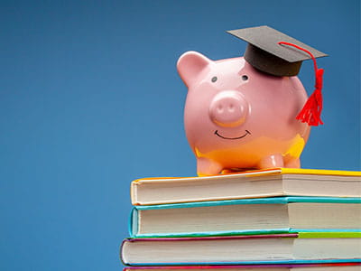 Piggy bank wearing graduation cap atop a stack of books