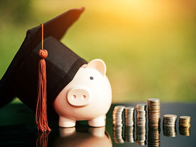 Piggy bank wearing graduation cap next to piles of coins to convey paying for college